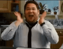 a man in a white shirt and tie is standing in a kitchen with his hands in the air .