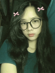 a girl wearing glasses and a blue shirt has two pink bows in her hair