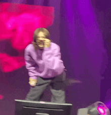 a woman in a purple sweater is standing on a stage in front of a monitor .