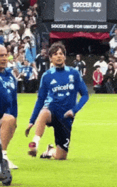 a soccer player wearing a blue unicef jersey kneeling on the field