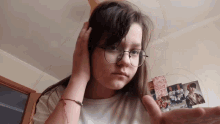a girl wearing glasses holds her hand out in front of a wall with pictures on it