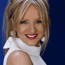 a woman wearing a white top and white earrings smiles