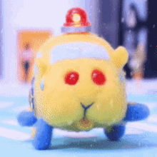 a yellow stuffed animal with red eyes and a red light on top is sitting on a blue surface .