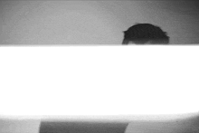 a black and white photo of a person peeking out from behind a table .