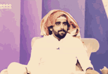 a man with a beard and a scarf around his head is sitting in a chair