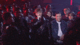 a man in a leather jacket is singing into a microphone while a crowd watches .