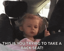 a little girl is sitting in a car seat holding a lollipop and saying this is you trying to take a back seat !