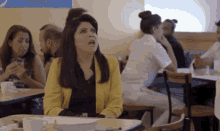 a woman in a yellow jacket is sitting at a table in a restaurant talking to a group of people .
