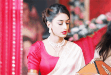 a woman in a red top and white saree is holding a box
