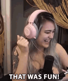 a woman wearing pink headphones is sitting in front of a microphone and laughing .