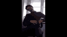 a man in a black jacket is holding a gun in front of a window