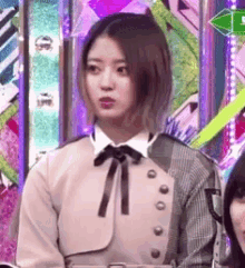 a woman wearing a jacket and a bow tie is standing in front of a colorful wall .