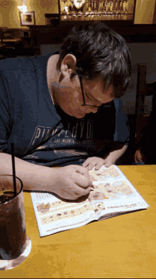 a man wearing a pink floyd shirt sits at a table looking at a menu