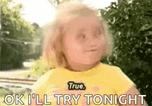 a little girl in a yellow shirt is standing in front of a tree and says `` ok i 'll try tonight '' .
