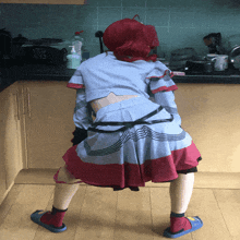 a woman in a blue and red dress is squatting in front of a kitchen counter