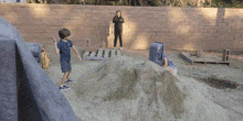 a boy and a girl are playing in a sandbox with a brick wall in the background .