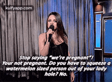 a woman is holding a microphone in front of a curtain and talking into it .