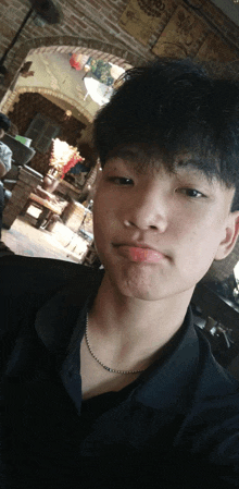 a young man wearing a black shirt and a chain around his neck takes a selfie