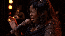 a woman singing into a silver microphone with a feather in her hair