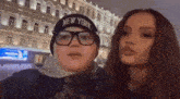 a boy wearing a new york hat and glasses is standing next to a woman .