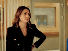 a woman in a black jacket is standing in a hallway with her hands on her hips