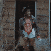 a woman in a hat and shorts is standing in a doorway holding a hammer .