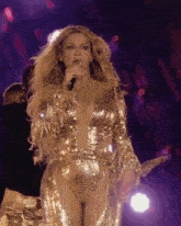 a woman singing into a microphone in a gold outfit