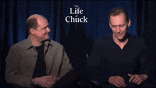 two men are sitting in front of a curtain that says the life of chuck on it