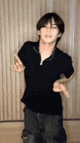 a young man in a black shirt is dancing in front of a window .