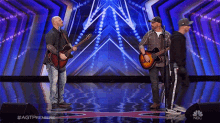 three men singing and playing guitars on a stage with a nbc logo in the corner