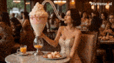a woman is sitting at a table holding a large ice cream sundae