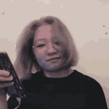 a woman wearing glasses and a black shirt holds a cell phone