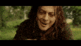 a man with long hair is making a funny face while sitting in the grass .