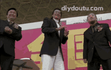 three men in suits are standing in front of a sign that says diydoutu.com