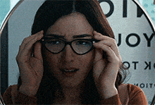 a woman wearing glasses looks at her reflection in a mirror