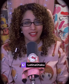 a woman with curly hair is wearing glasses and a pink hello kitty sweatshirt with a latinaotaku sticker