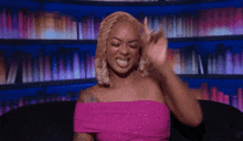 a woman in a pink dress is sitting on a couch making a funny face .