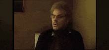 a man with glasses and gray hair is sitting in a dark room .