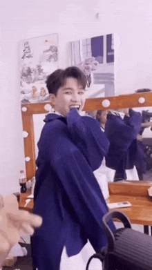 a young man in a blue jacket is standing in front of a mirror and smiling .