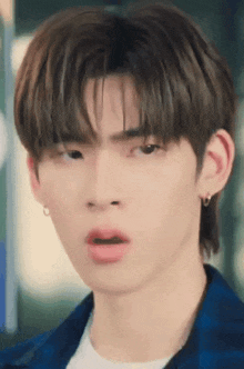 a young man with a surprised look on his face is wearing a blue plaid shirt and earrings .