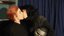 a man with red hair kisses another man with black gloves