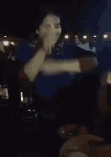 a woman in a blue shirt is shaking hands with another woman in a dark room