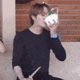 a young man is drinking from a bowl with chopsticks