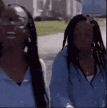 two women wearing blue shirts and glasses are standing next to each other on a street .