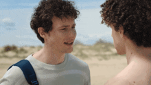 a man with curly hair is talking to another man without a shirt