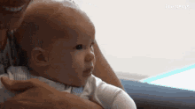 a person is holding a baby in their arms and the baby is looking at something .