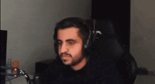 a man with a beard is wearing headphones while sitting in a chair in front of a microphone .