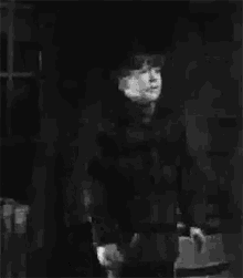 a black and white photo of a young boy in a jacket standing in a dark room .