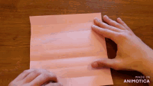 a person folding a piece of pink paper on a wooden table