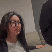 a woman wearing glasses is sitting on a couch looking at a man .